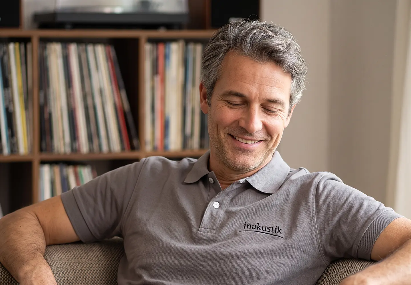 Man wearing the in-akustik polo shirt, sitting on a sofa and listening to music