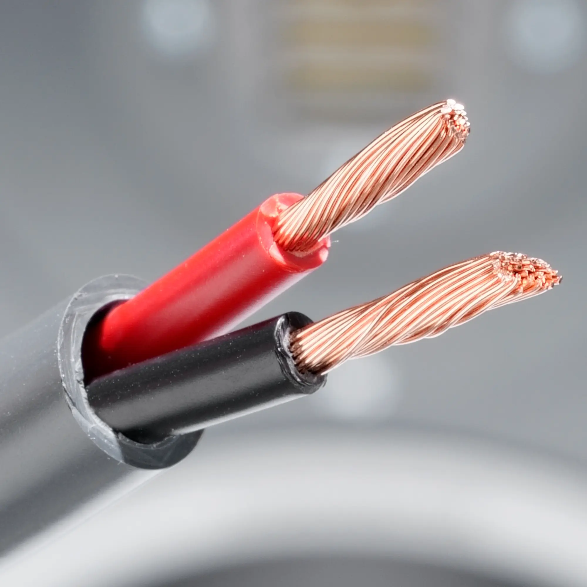 Close-up of the flame-retardant speaker cable with exposed strands, with a speaker in the background.