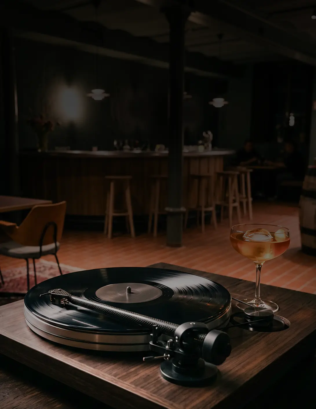 Plattenspieler mit Cocktailglas im Vordergrund, im Hintergrund Barbereich mit Hockern.