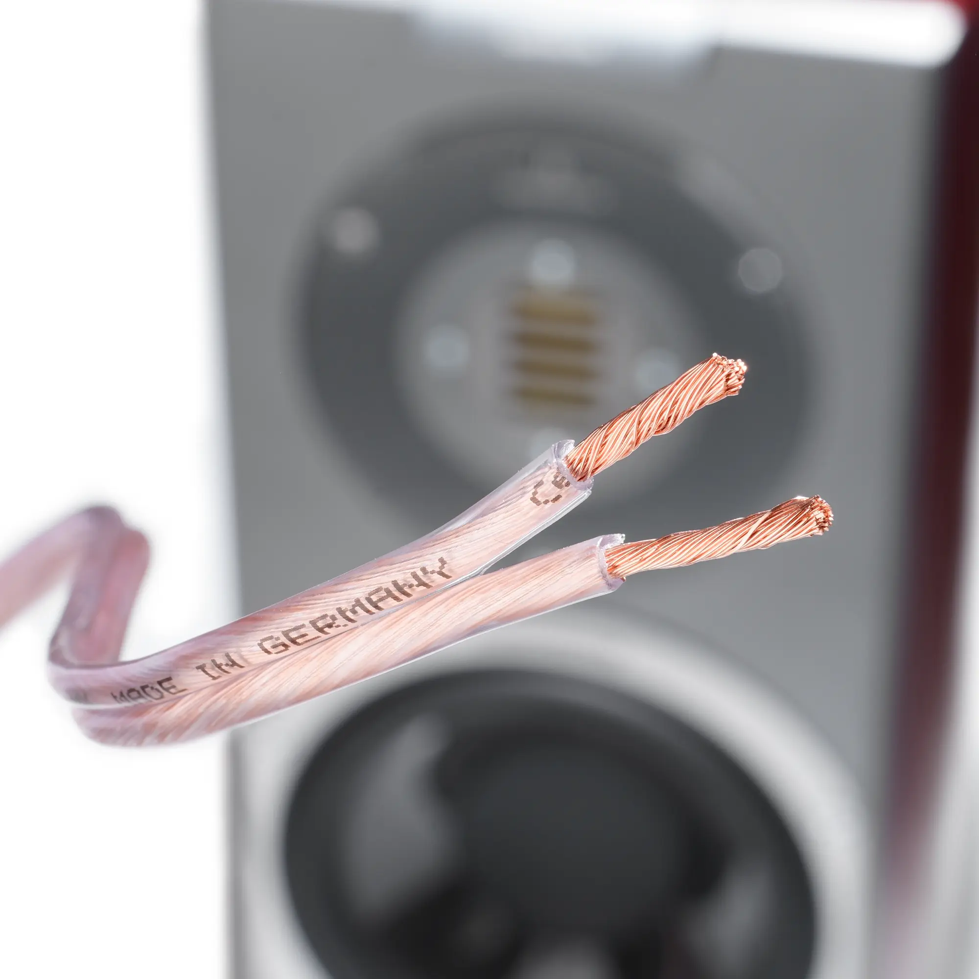 Close-up of a bare copper cable with exposed copper wires, with a speaker in the background.