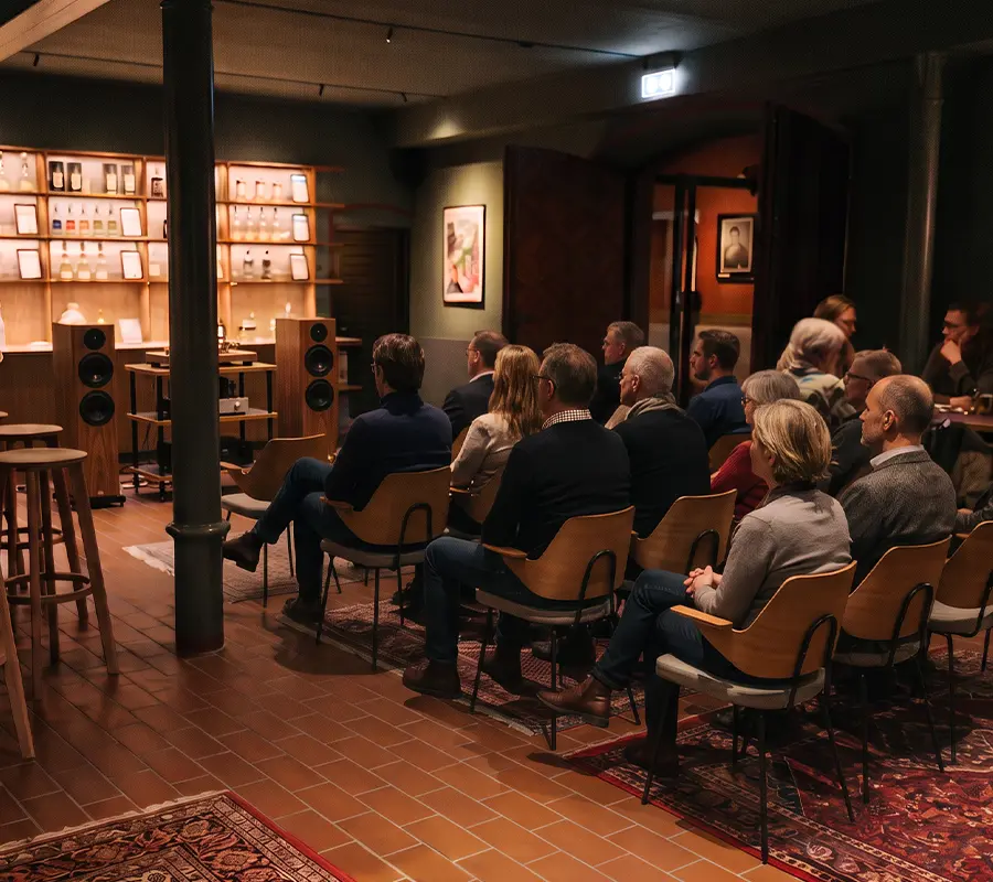Gruppe sitzender Menschen in einem Raum mit in-akustik HIFI-Anlage und Regalen im Hintergrund