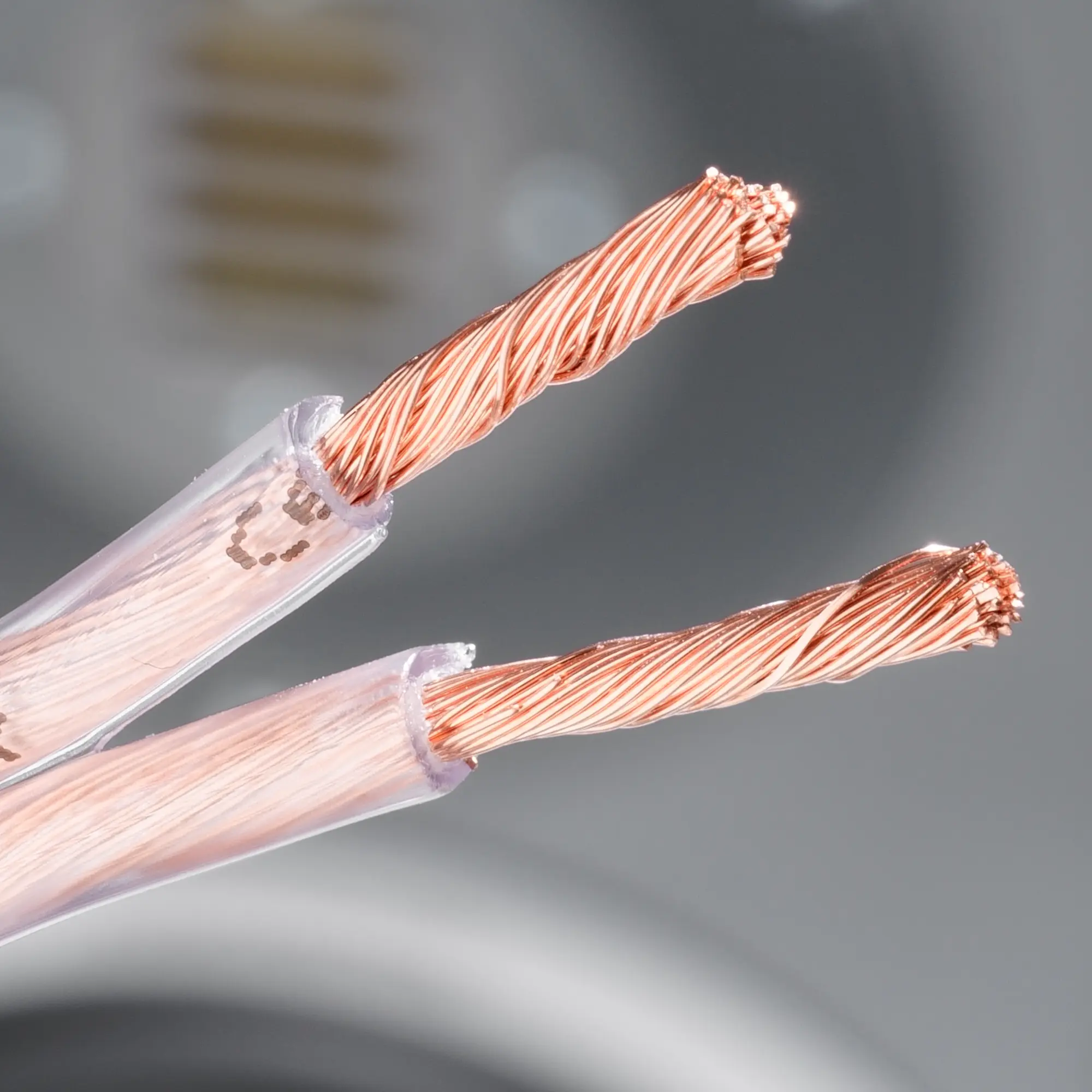 Close-up of a bare copper cable with exposed copper wires, with a speaker in the background.