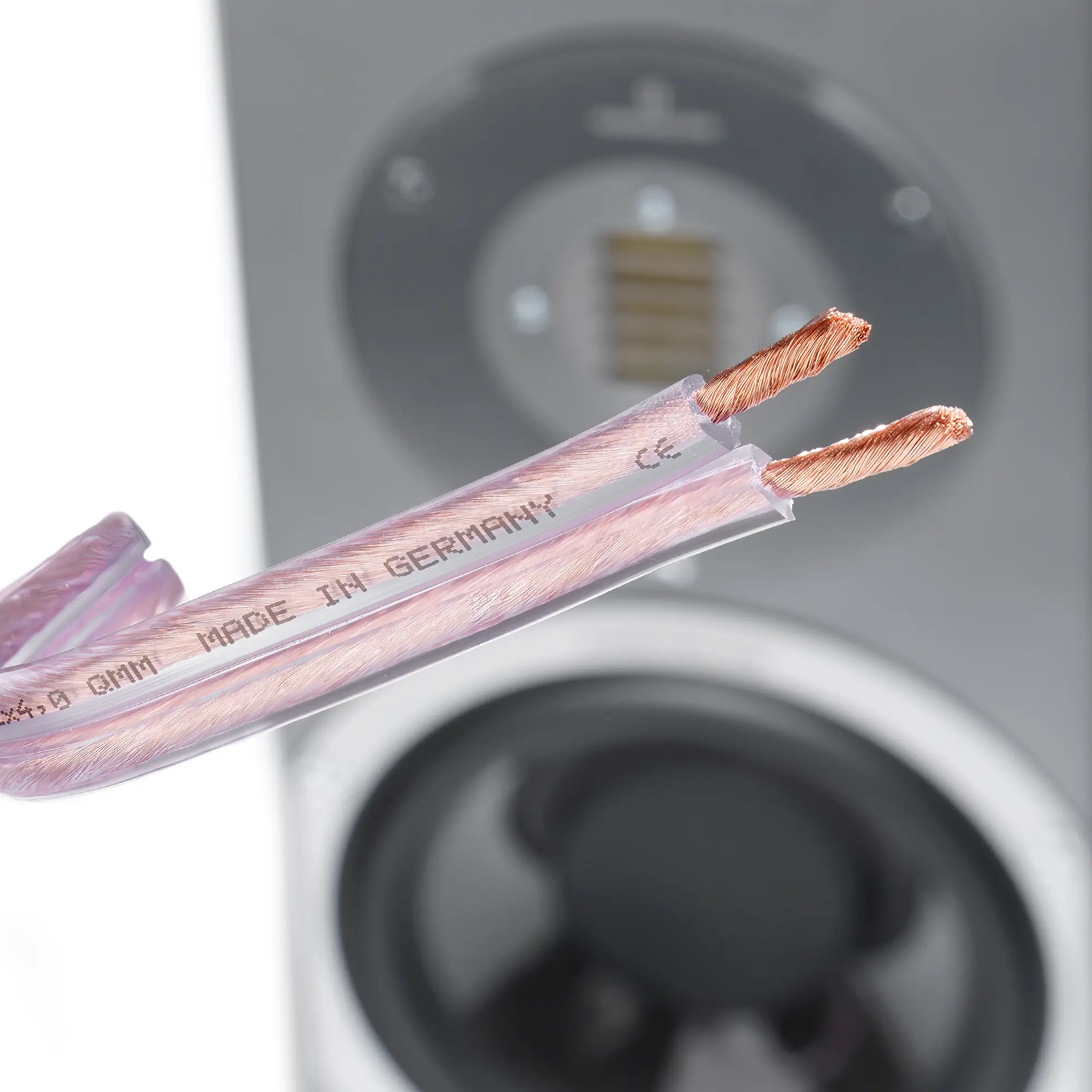 Close-up of the premium copper cable with exposed copper wires, with a speaker in the background.